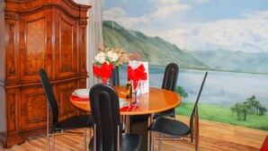 A dining area with a round table, black chairs, a wooden cabinet, and a scenic mural on the wall.