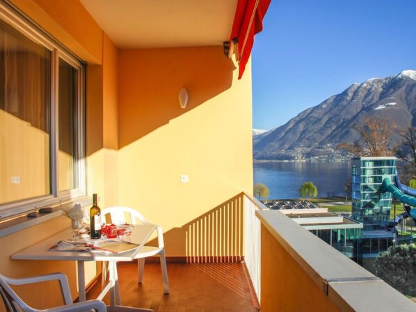 A balcony with a table and chairs, overlooking a lake and mountains.