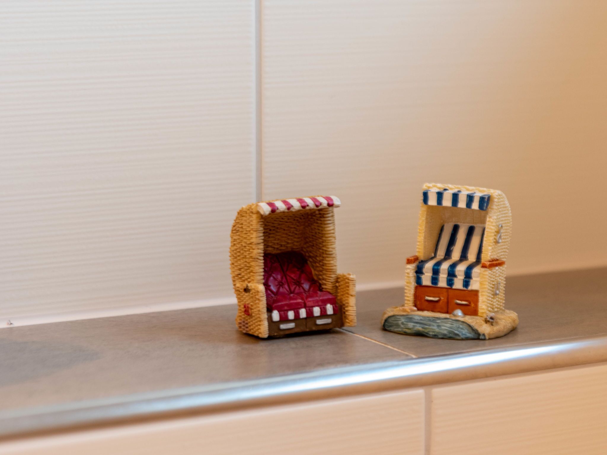 Two miniature chairs with striped patterns and a red cushion, placed on a shelf.