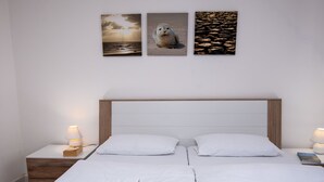 Cama bem arrumada com roupa de cama e toalhas brancas, cabeceira de madeira e mesas de cabeceira com luminárias.