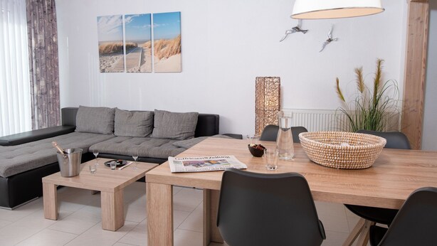 Uma sala de estar moderna com teto de madeira, um sofá cinza, uma mesa de jantar com cadeiras e uma janela grande com cortinas.