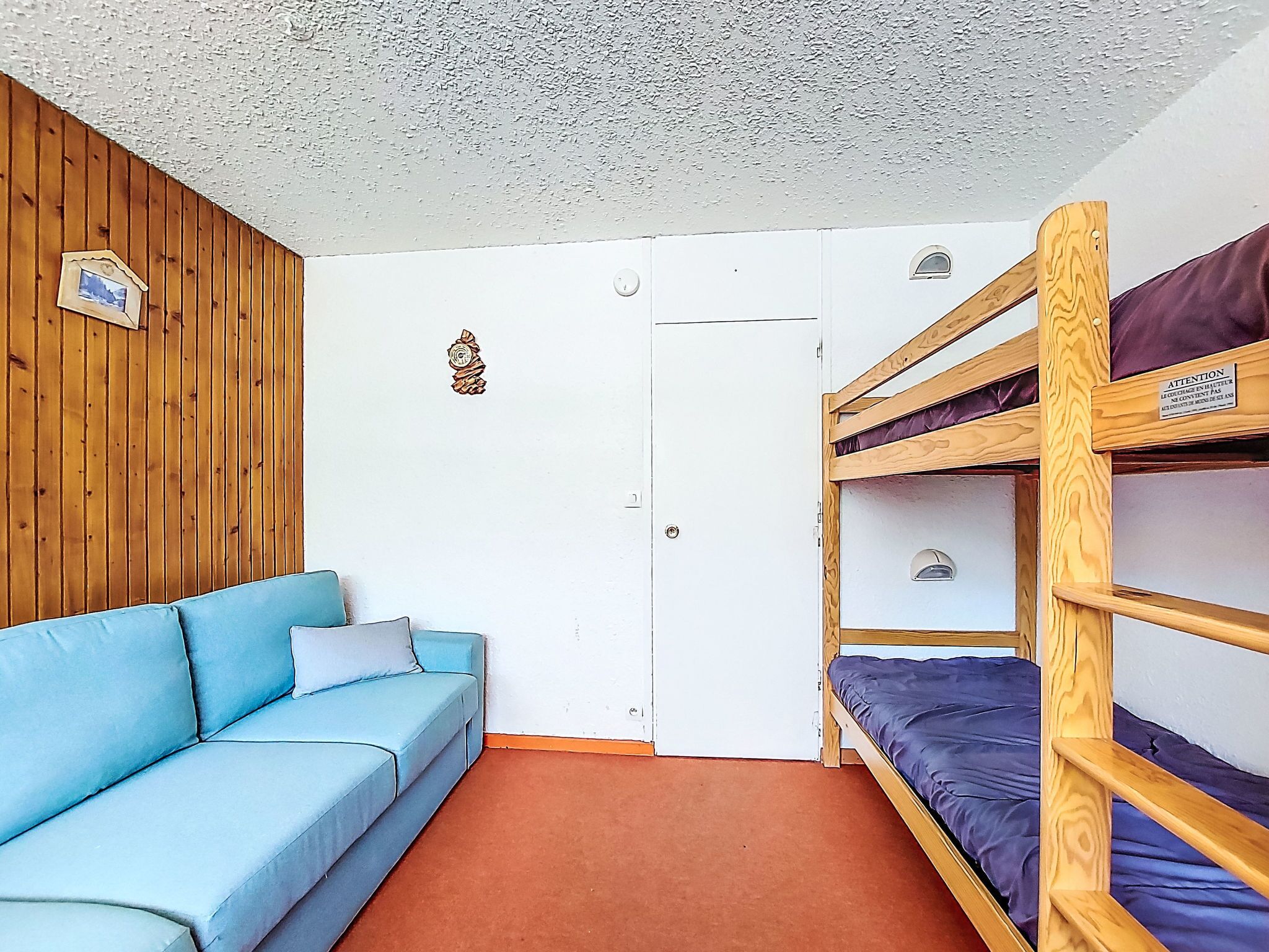 Una habitación con una cama litera, un sofá, una puerta y una pared de madera.