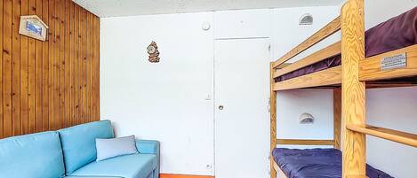 Una habitación con una cama litera, un sofá, una puerta y una pared de madera.