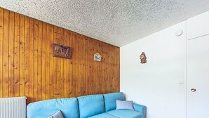 A room with a blue sofa, wooden panel wall, white door, and a radiator. - Aravis 101 by Interhome (Les Menuires)