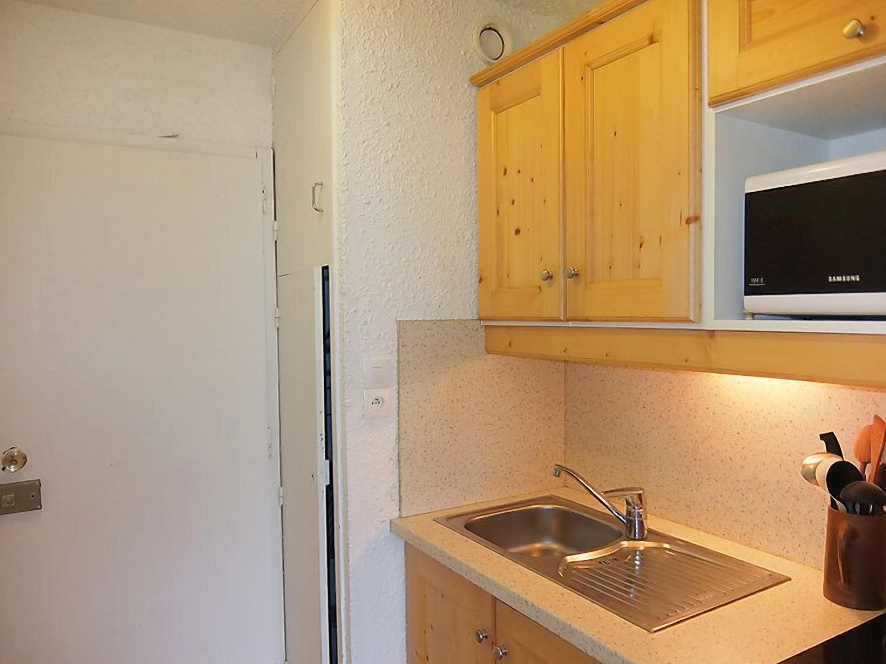 A kitchen with wooden cabinets, a stainless steel sink, and a microwave above the counter.