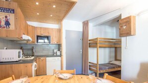 A compact kitchen with wooden cabinets, a microwave, and a dishwasher. There is a dining table set with plates, glasses, and a cake. A bunk bed is visible in the background. - Le Curling A (Val Claret) by Interhome (Tignes)