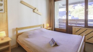 A bedroom with a wooden bed, a bedside table with a lamp, a window with a view of a mountain, and a wooden wall decoration. - Le Curling A (Val Claret) by Interhome (Tignes)