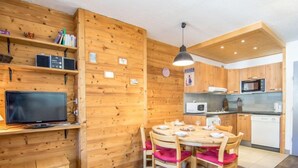 A wooden interior with a dining table and chairs, a television, and kitchen appliances. - Le Curling A (Val Claret) by Interhome (Tignes)