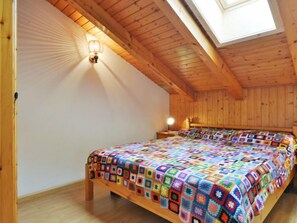 A cozy attic bedroom with a wooden ceiling, a skylight, a colorful quilt, and a bedside lamp.