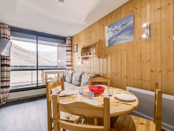A cozy room with a wooden interior, a round wooden table with chairs, a sofa, and a large window offering a view of the outdoors.