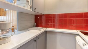 Ett modernt kök med vita skåp, en röd kakelvägg bakom arbetsbänken och en inbyggd diskmaskin.