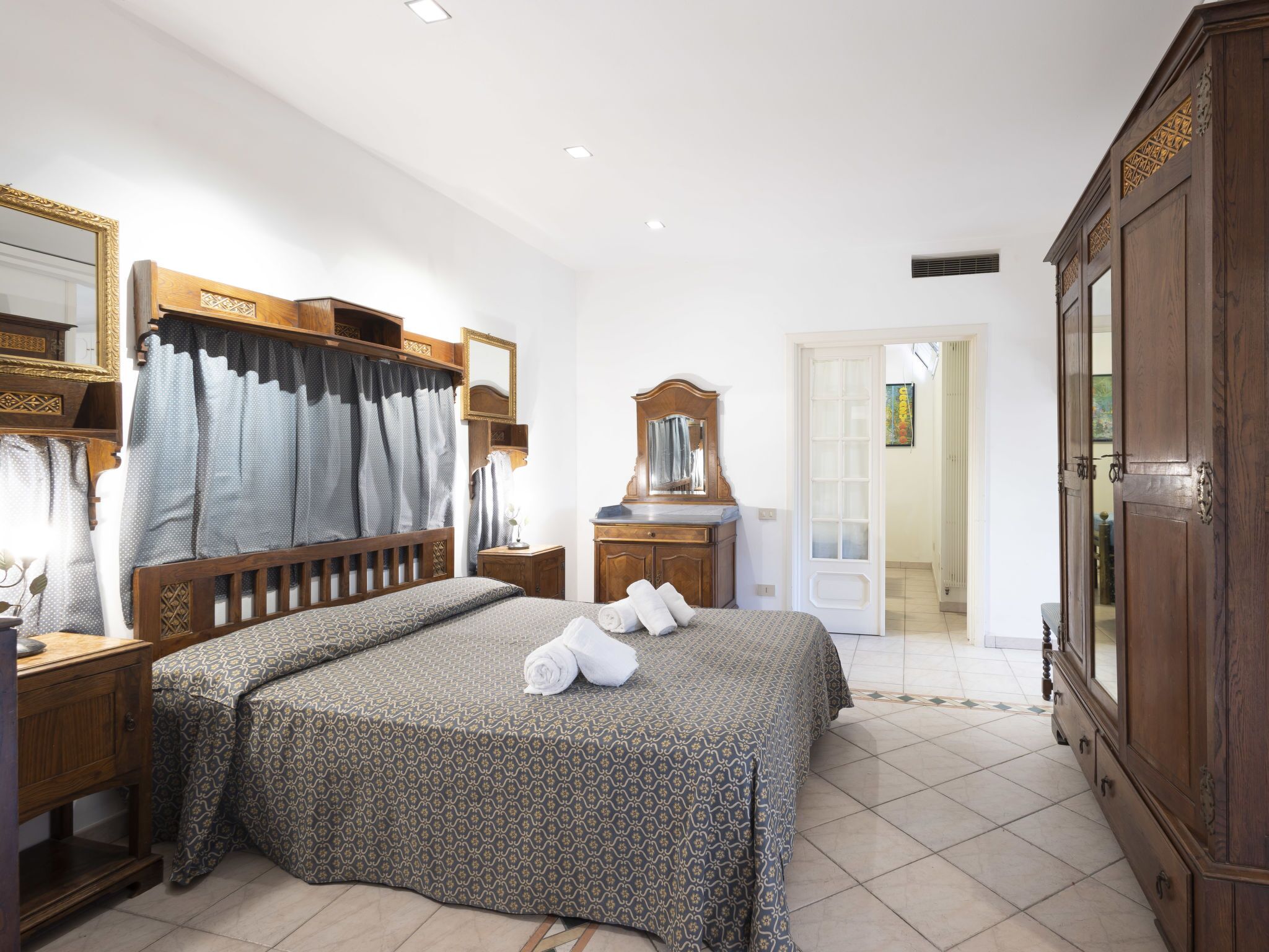 A hotel room with a large bed, wooden headboard, a dresser, a mirror, and a wardrobe.