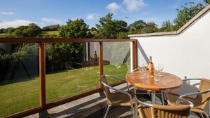 A patio with a round wooden table and wicker chairs, overlooking a grassy area and trees. - Villa Gallery by Interhome (Truro)