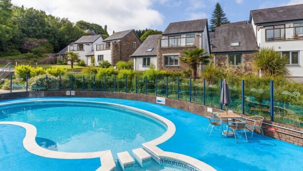 A swimming pool with a wavy design, surrounded by a fence and a row of houses in the background. - Villa Gallery by Interhome (Truro)