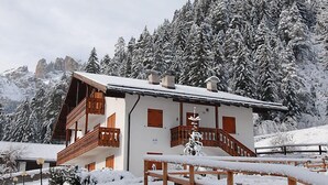 Un chalet doté d’un balcon en bois, d’un escalier et offrant une vue sur des arbres et des montagnes enneigés.