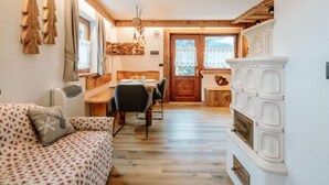 Une pièce chaleureuse avec un plafond en bois, un coin repas comprenant une table et des chaises en bois, un canapé recouvert d’un tissu à motifs et un meuble blanc agrémenté d’éléments décoratifs.