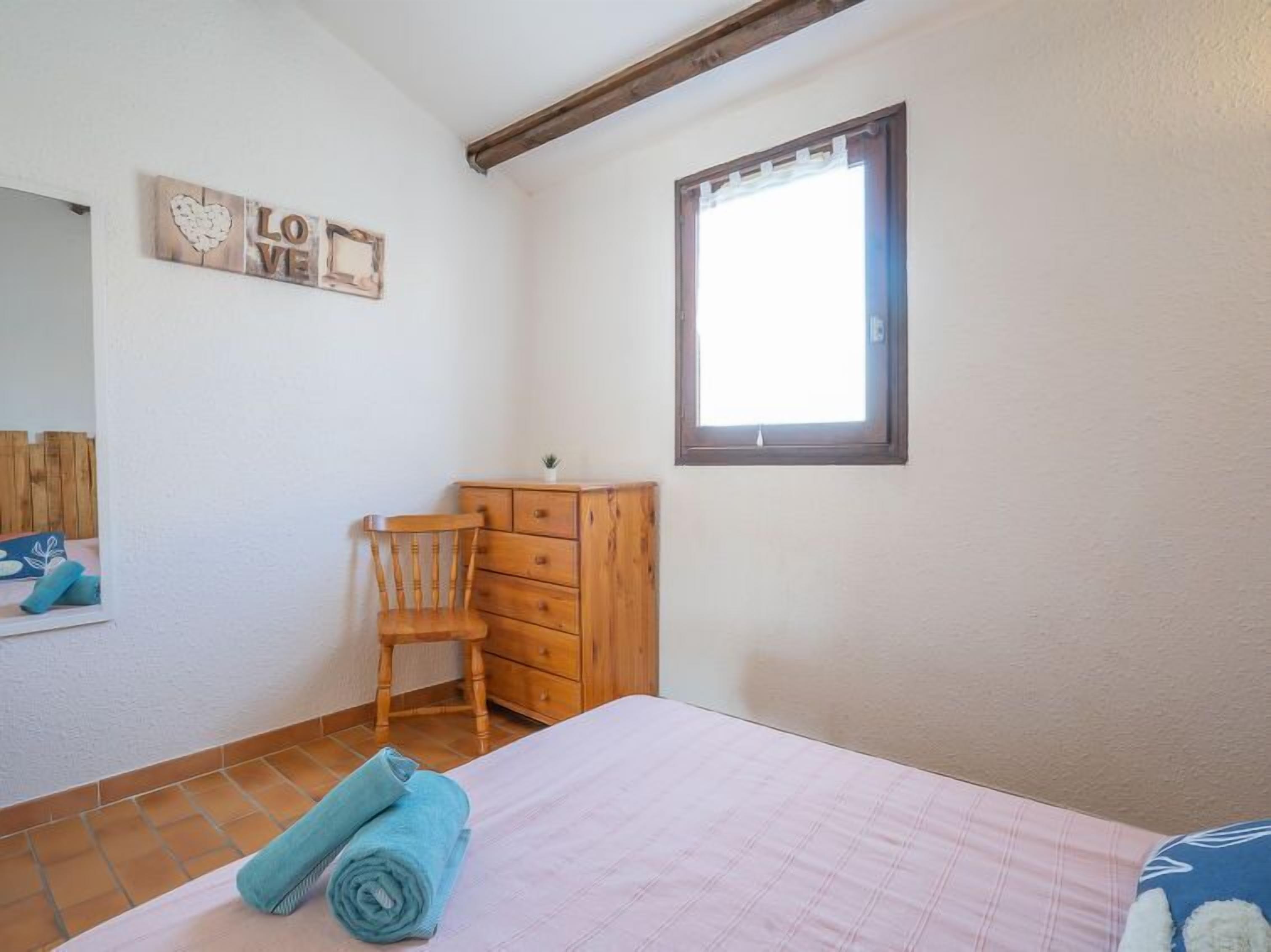 Une chambre à coucher avec un lit, une commode en bois, une chaise et une fenêtre.