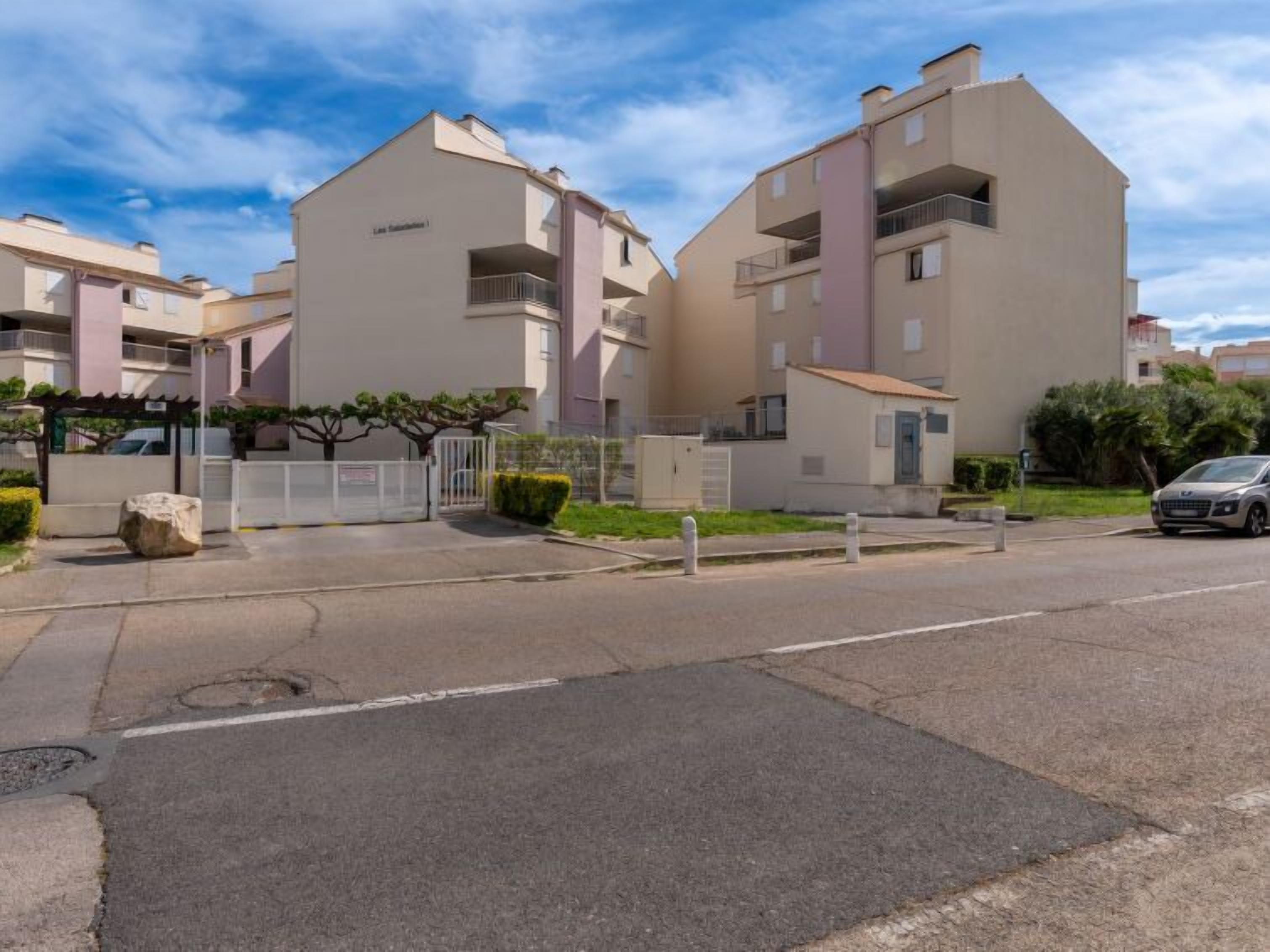 A modern apartment complex with multiple buildings, balconies, and a gated entrance.