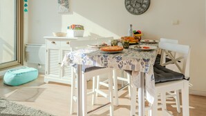 Un coin repas avec une table dressée pour quatre personnes, une horloge au mur et une fenêtre avec des stores.