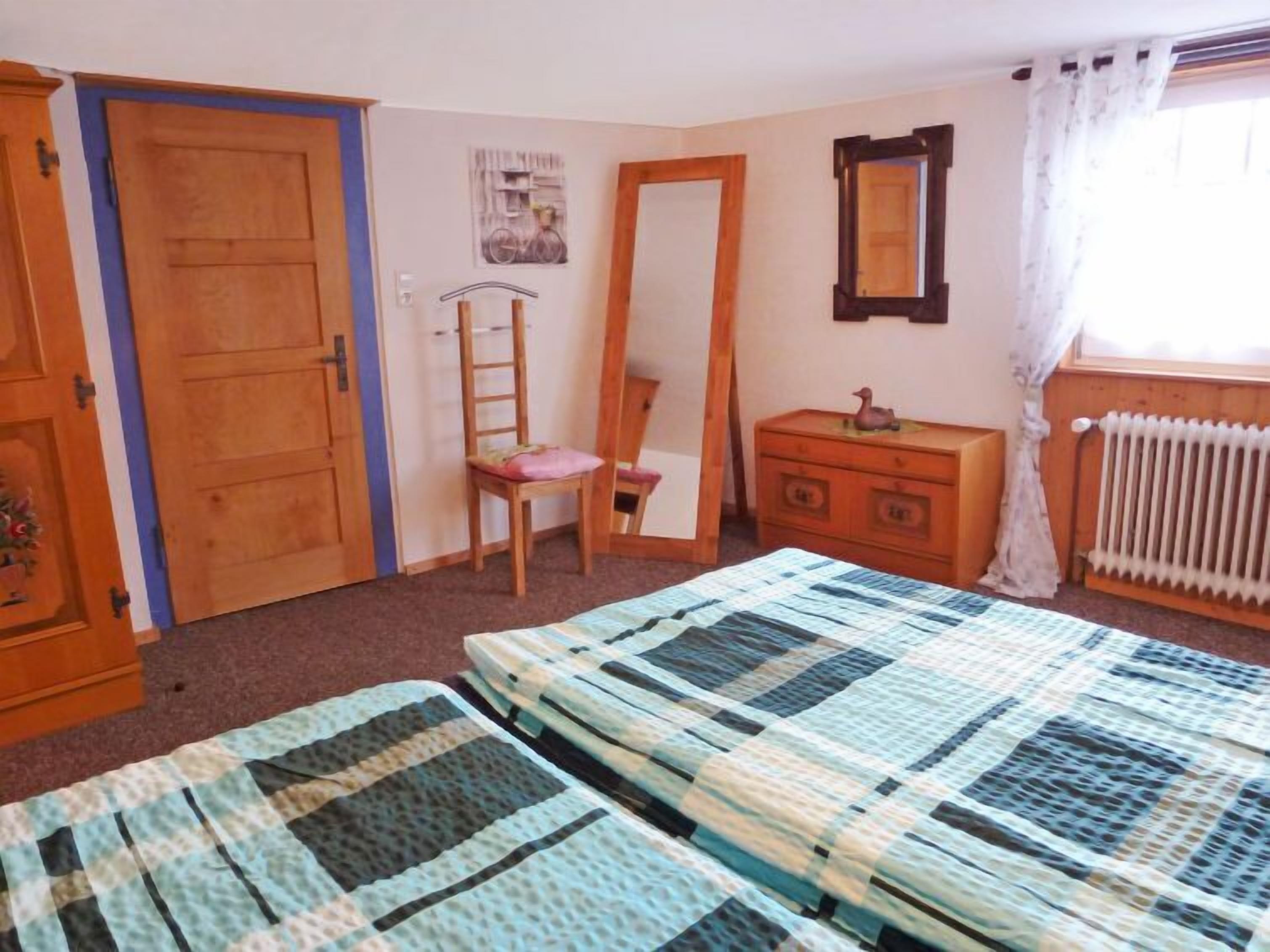 Una camera da letto con due letti, una cassettiera, una sedia, uno specchio e un termosifone.