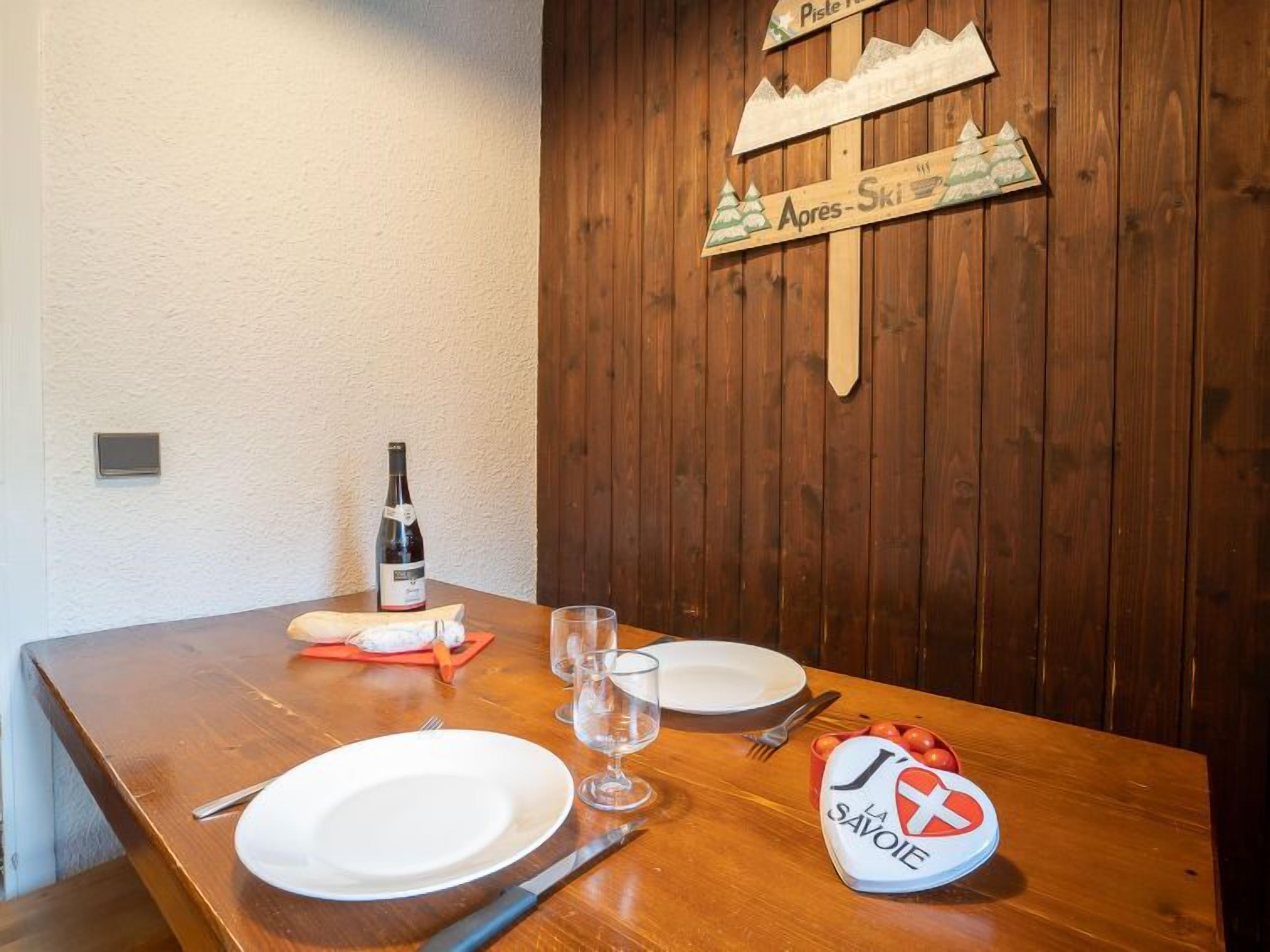 A wooden dining table with a bottle of wine, glasses, plates, and cutlery. A wooden sign with mountain graphics is on the wall.