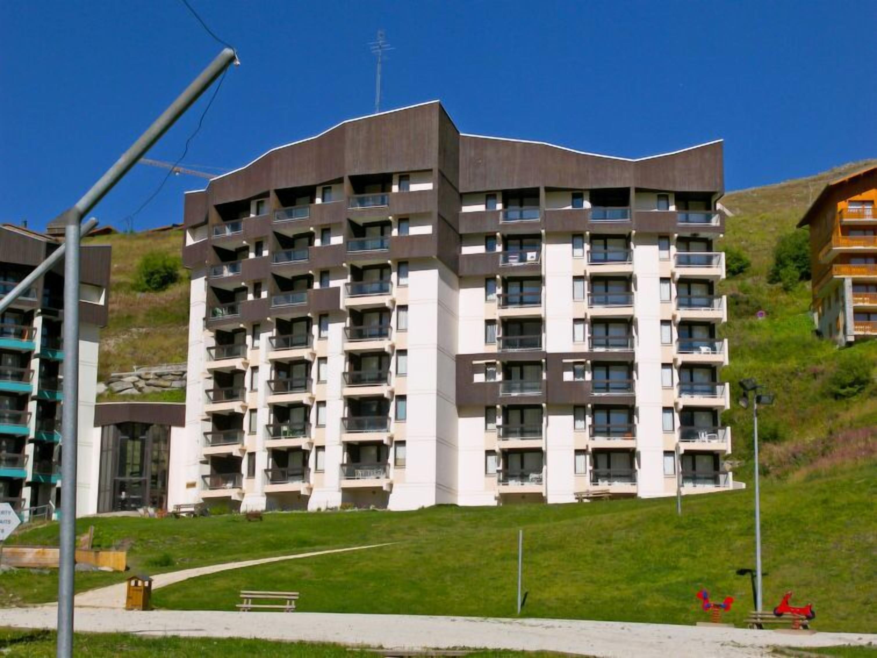 A multi-story residential building with balconies, situated on a grassy slope.