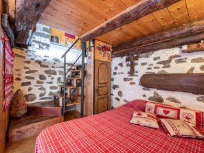 Een knus vertrek met een stenen muur, een houten trap en een bed met rode beddengoed.