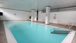 An indoor swimming pool with a clear water surface, white walls, and a bench along the side. - Alpenland by Interhome (Seefeld in Tirol)