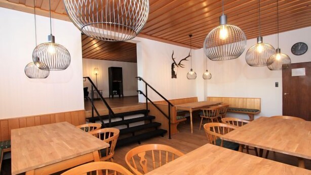 A restaurant interior with wooden tables and chairs, a staircase, and hanging pendant lights. - Alpenland by Interhome (Seefeld in Tirol)