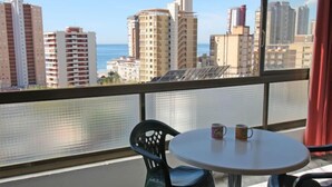 Ein Balkon mit Blick auf eine Stadtlandschaft und das Meer. Ein runder Tisch mit zwei Tassen und zwei Stühlen.