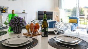 Une table à manger dressée avec des assiettes, des verres et une bouteille de vin, offrant une vue sur l’extérieur grâce à une grande fenêtre.