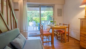 Ein gemütliches Zimmer mit einer Couch, einem Esstisch mit Stühlen und Gartenblick durch eine Schiebetür.