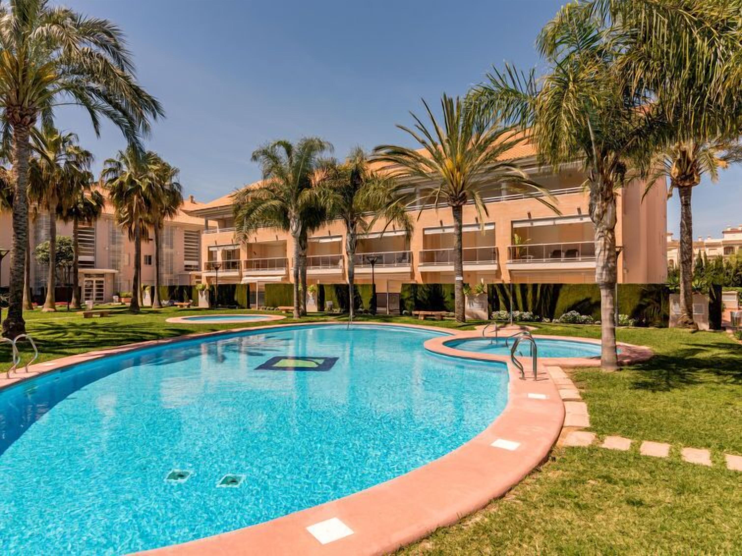 Una piscina dalle linee curve, circondata da palme e un edificio con numerosi balconi.