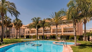 Ein Pool mit geschwungener Form, umgeben von Palmen und einem Gebäude mit mehreren Balkonen.