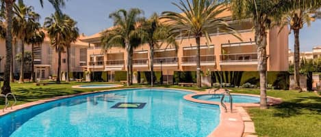 Una piscina de diseño curvo, rodeada de palmeras y un edificio con varios balcones.