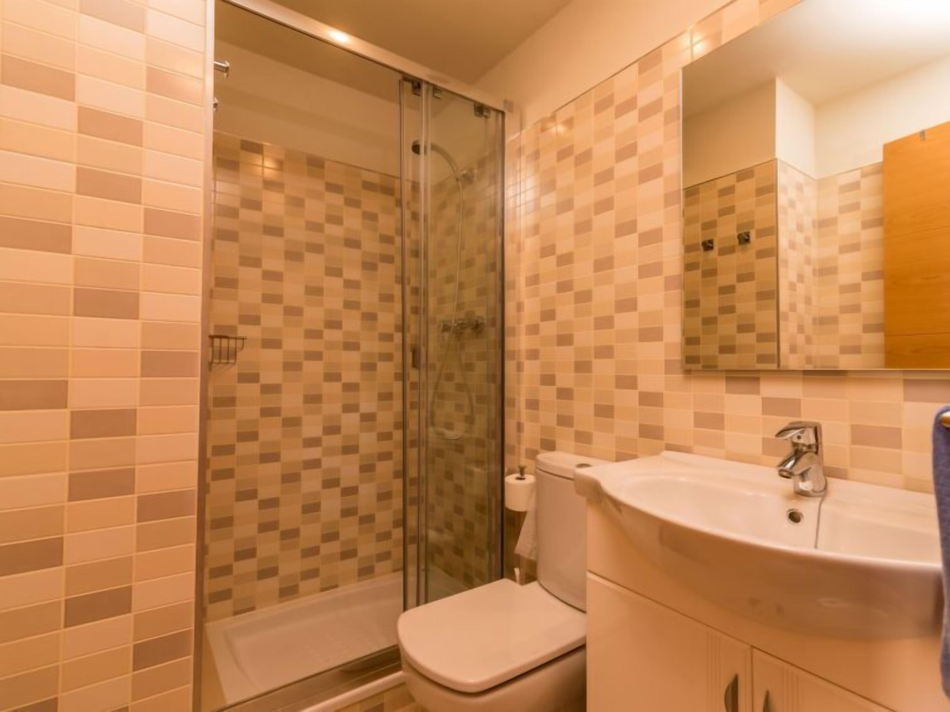 A bathroom with a glass shower enclosure, a toilet, and a sink with a mirror above it.