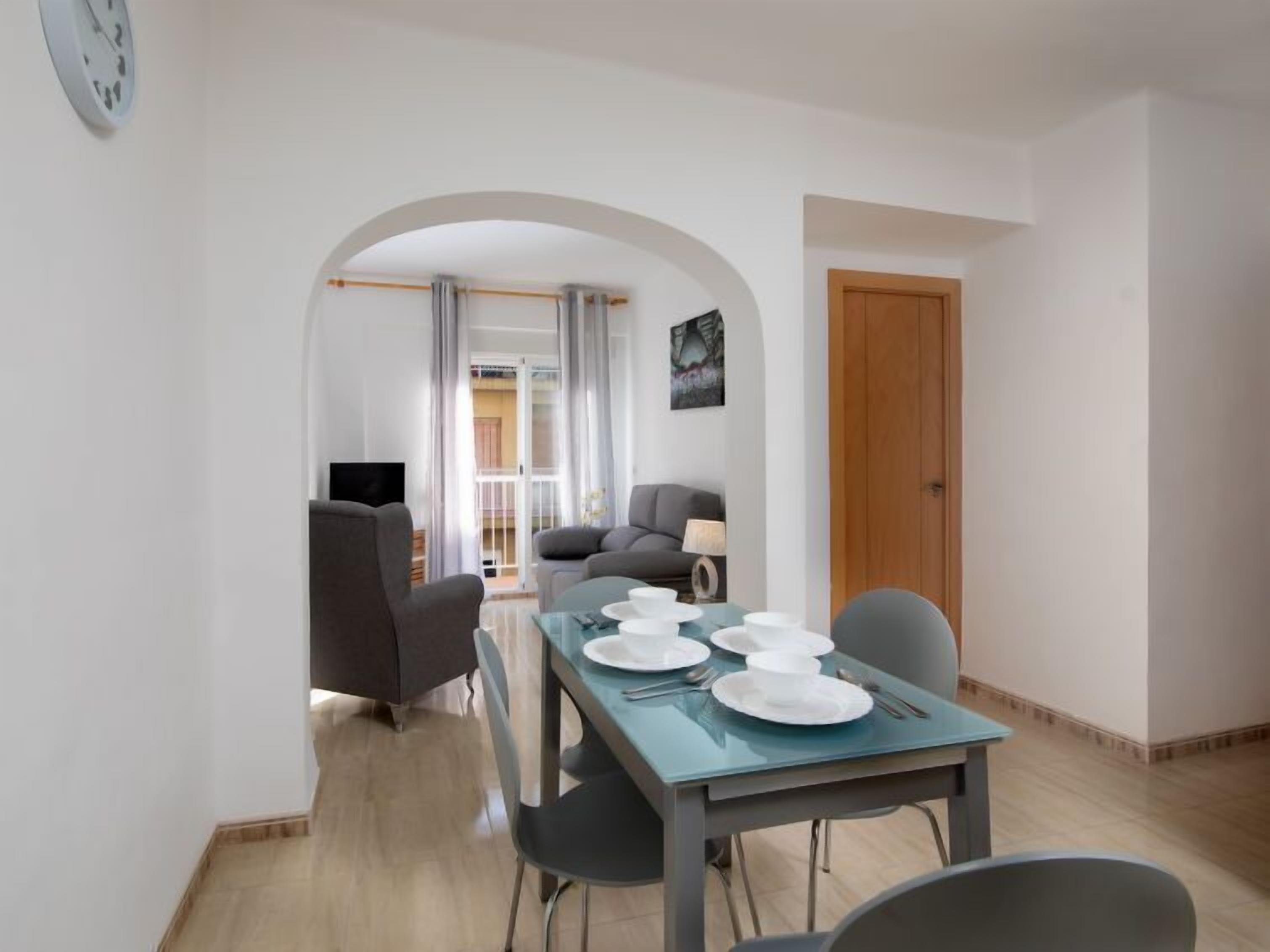A dining area with a table set for four, a sofa, a TV, and a door.