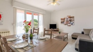A dining area with a wooden table set for four, a ceiling fan, and a TV on a stand. - Les Mimosas by Interhome (Saint Aygulf)