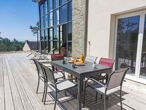 Une terrasse dotée d’une table et de chaises, offrant une vue sur un mur en pierre et une porte vitrée donnant sur un patio.