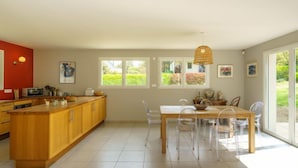 Una cocina moderna con armarios de madera, una mesa de comedor con sillas y grandes ventanales con vistas a zonas verdes.
