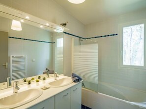 Une salle de bain moderne avec deux lavabos, un grand miroir, un porte-serviettes et une baignoire.