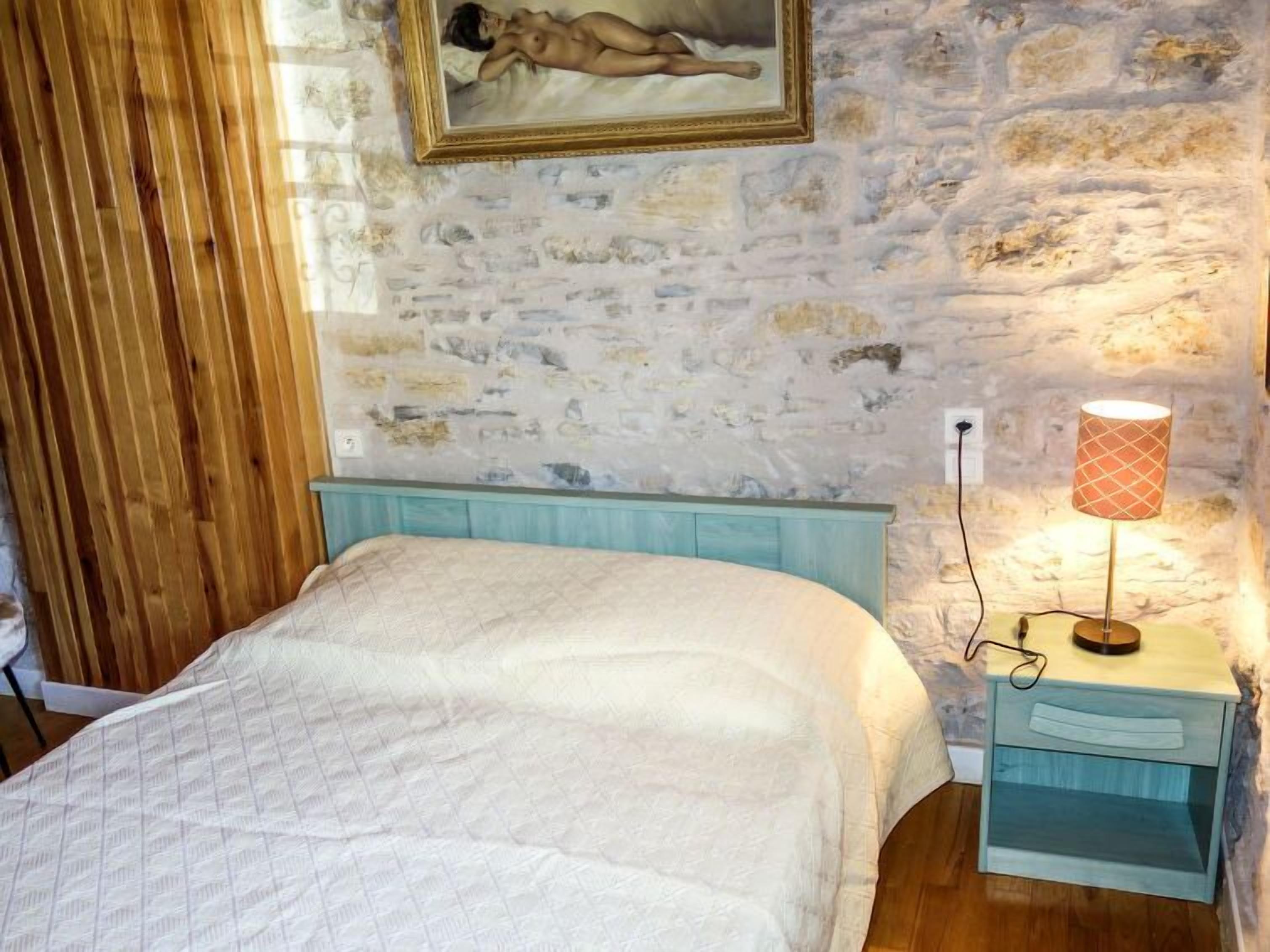 A bedroom with a bed, a nightstand, a lamp, and a painting on the wall.
