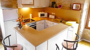 Eine kleine Küche mit weißen Schränken, einer Mikrowelle, einem Toaster und einem Spülbecken. Zwei Stühle und eine kleine Kücheninsel mit einer Blumenvase.