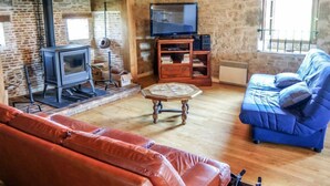 Ein Wohnzimmer mit Backsteinwand, Kamin, Fernseher, blauem Sofa und einem roten Ledersessel.