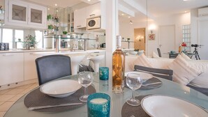 A modern dining area with a glass table set for four, surrounded by a kitchen and living space. - Le Cheverny by Interhome (Cannes)