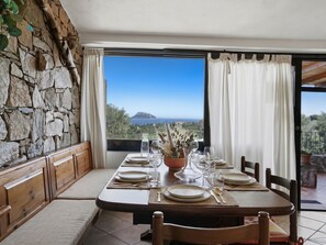 A dining area with a table set for four, a stone wall, and a view of the sea.
