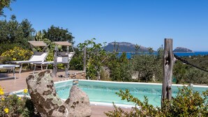 A pool area with lounge chairs, a wooden deck, and a view of the sea and a mountain. - Vacation home Iride by Interhome (Golfo Aranci)