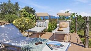 Two sun loungers with cushions, a book, and sunglasses on a table, surrounded by greenery and a view of the sea. - Vacation home Iride by Interhome (Golfo Aranci)