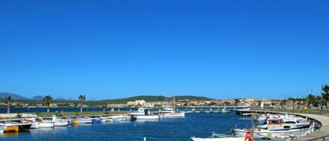 A marina with various boats docked, a clear blue sky, and a hilly landscape in the background.