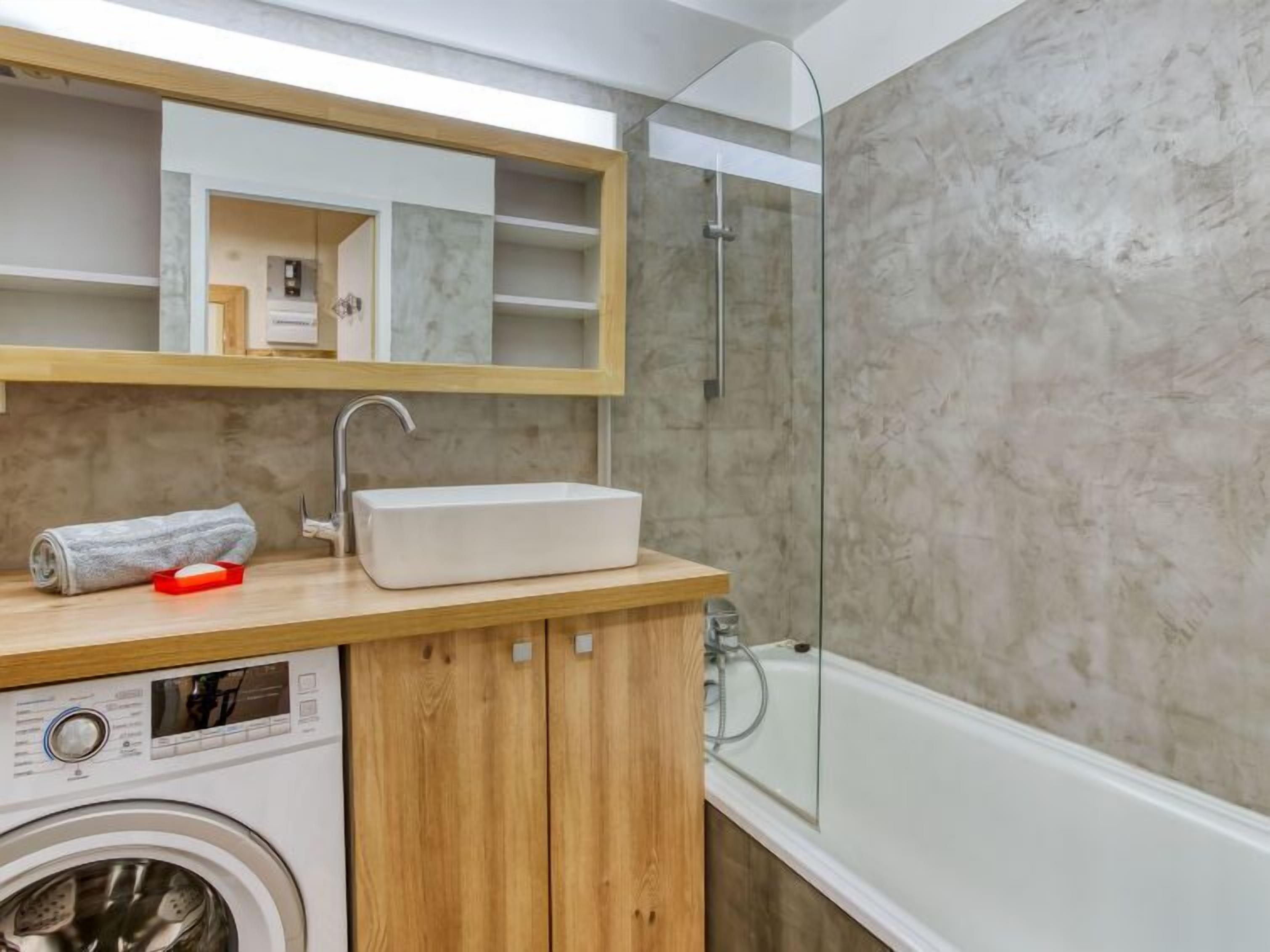 Un baño moderno con lavadora integrada, lavamanos y ducha con mampara de vidrio.